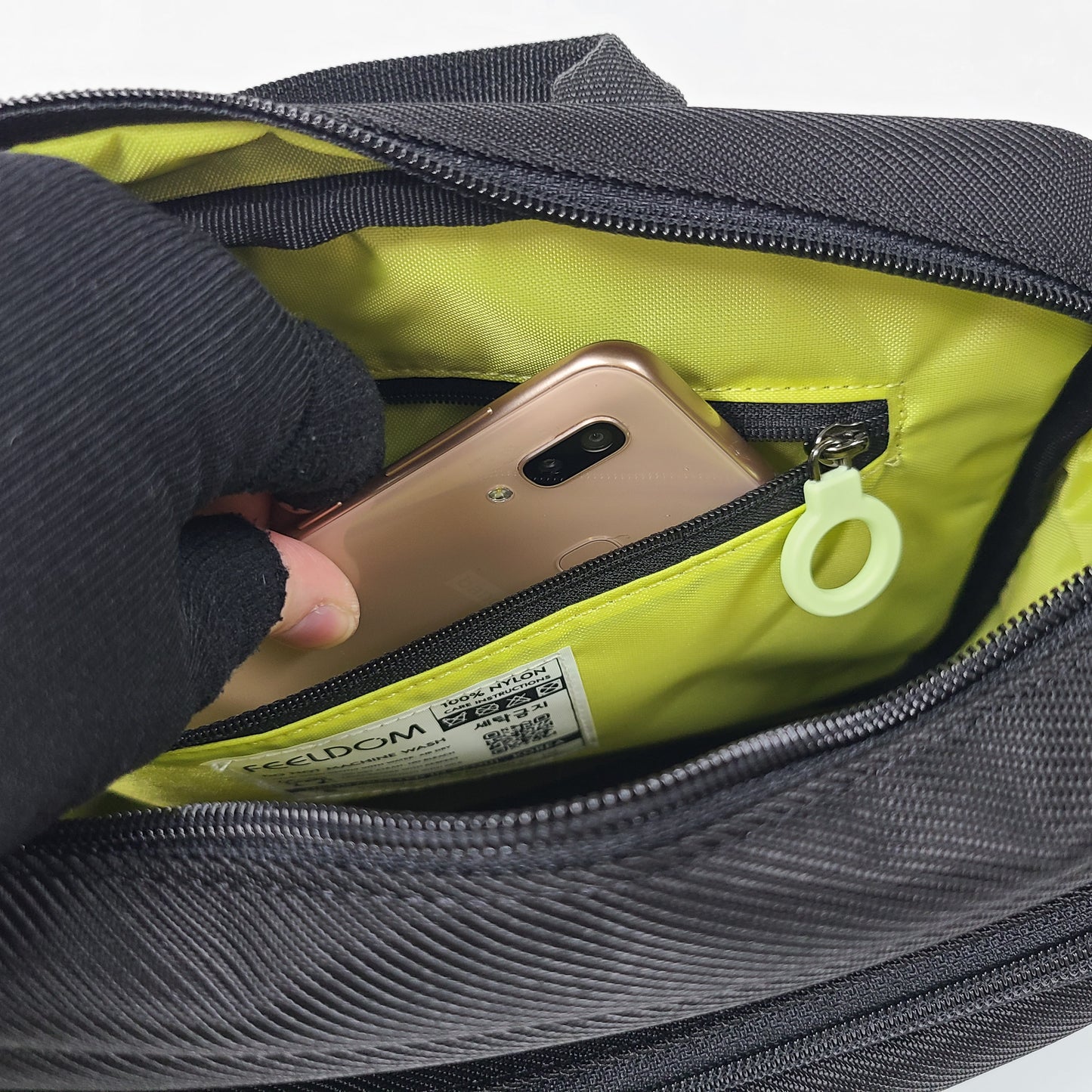 Close up of a hand putting a smartphone into the inner zipper pouch of the satchel . The lining is yellow and the zipper ring is white.