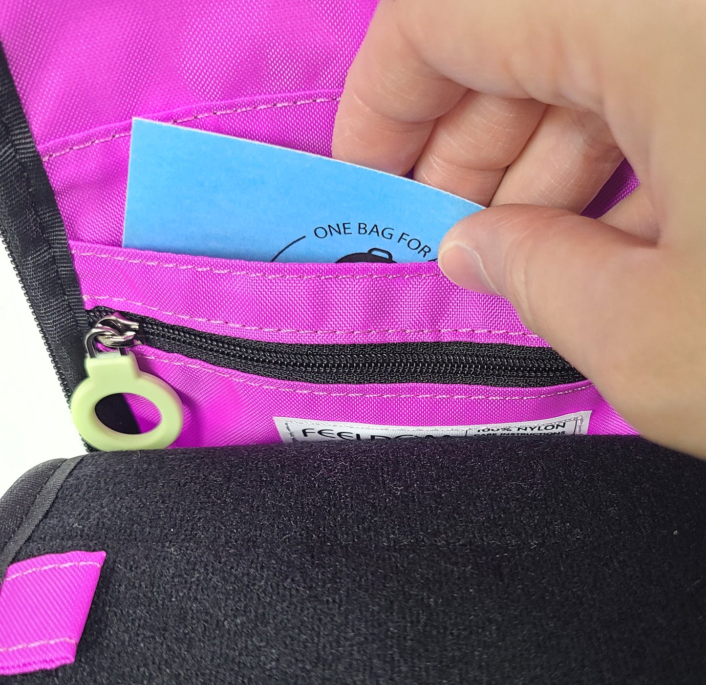 Close up detail of someone putting a 3 x 5 inch badge into the inner badge slot, so that the badge will show through the clear plastic window on the front. The inner side of the badge slot is also a zipper pocket.