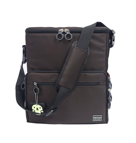 Front view of a square shoulder bag, dark brown, with a removable padded shoulder strap and black trim and black ring zippers on the top lid. There is a glow in the dark dog character keychain attached to the front zipper. There are 2 front pockets.