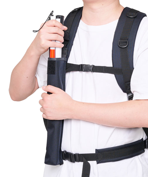 A person is wearning a backpack, front view, showing the attached waist belt and chest straps. They are taking out the white cane from the cane pouch which is attached to the D ring on the right backpack strap.