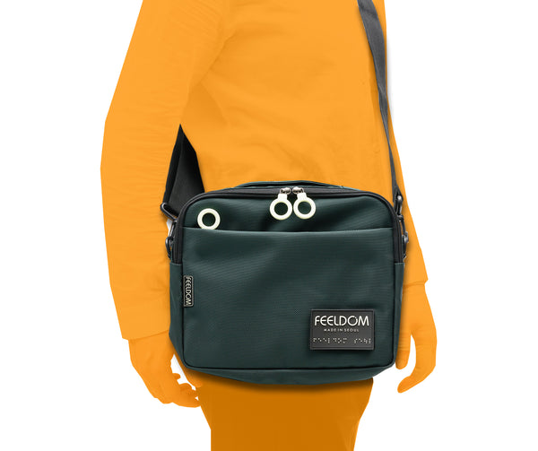 The Tekno Pouch S-Series is a medium rectangular shaped  pouch with a handle and a detachable shoulder strap. It has large zipper rings and a glow in the dark FEELDOM Logo braille patchIt can be worn as a crossbody or attached to a mobility device or backpack.