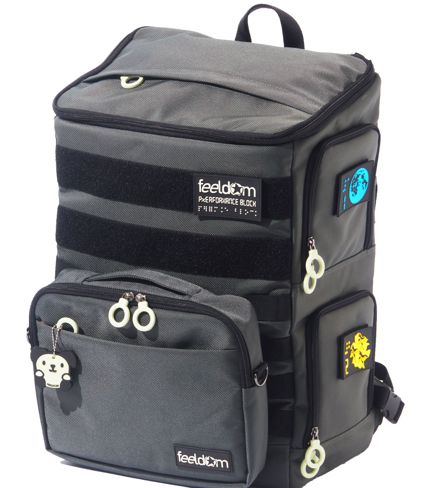 A large backpack with side openings. Gray ballistic nylon with white zipper rings and bright braille patches on the side. There is a zipper on the top with a rain cover. There is an additional pouch attached to the front. This TEKNO Pouch is sold separately. Glow in the dark labels read FEELDOM.