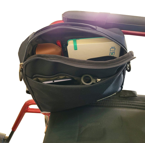 Tech Pouch attached to the arm of a wheelchair. It is open, and there is a diary, sunglasses, pens and cellphone in the various pockets.