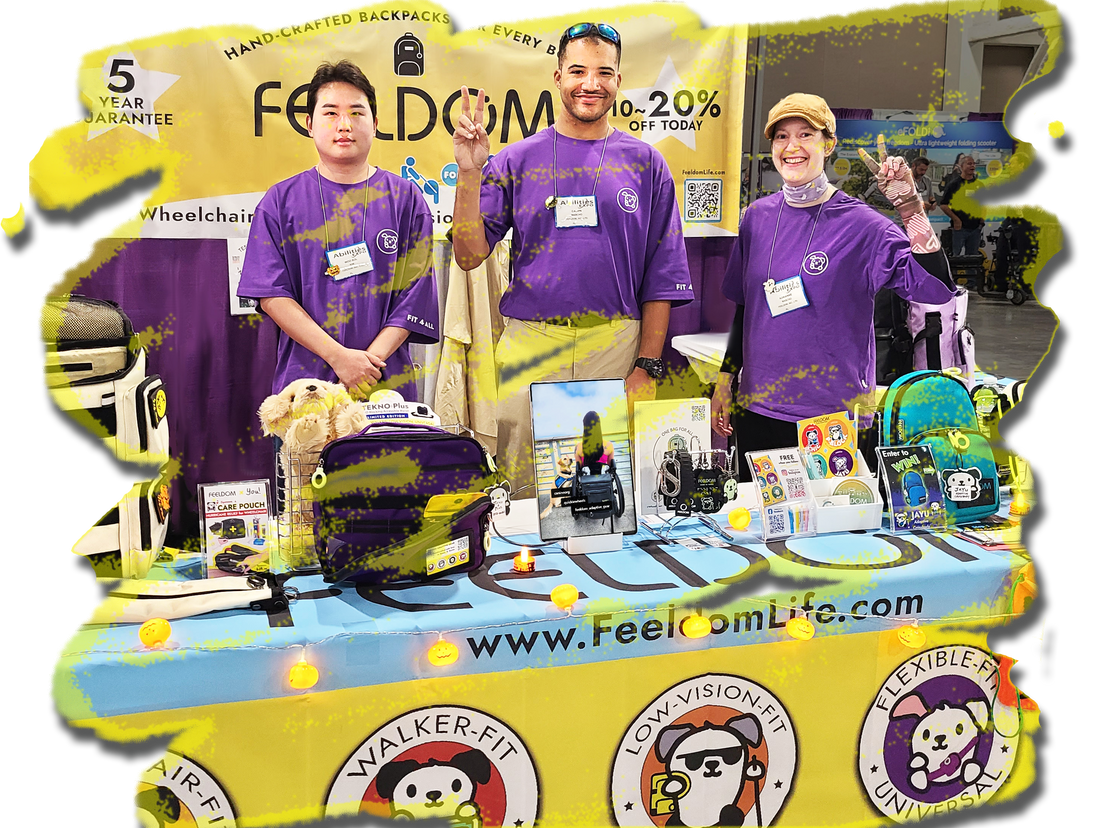3 smiling people wearing purple FEELDOM logo t-shirts are standing in front of a Yellow FEELDOM banner and there's a yellow table banner with many small items displayed on it.