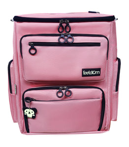 Large Box shaped wheelchair bag that looks like a suitcase, light pink with black double ring zippers on the flip top lid and outer pockets.