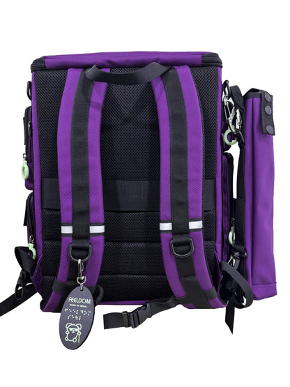 Backside of a Purple backpack with a cane pouch attached to the side. Backpack has a black padded backside, shoulder straps and waist strap with reflective accents and Braille Keychain attached to the D-ring.