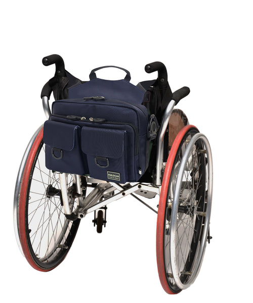 A rectangular wheelchair bag with two front pockets is attached to the back of a manual wheelchair