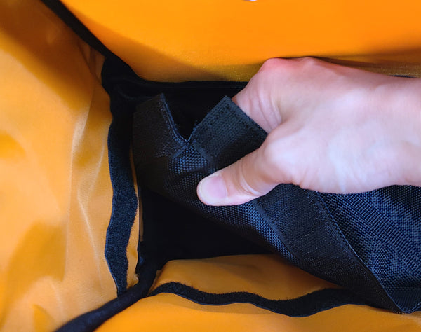 A bright orange inner lining. A removable divider separates the upper and lower compartments. Someone is removing it by peeling away the divider from the inner walls of the backpack. 