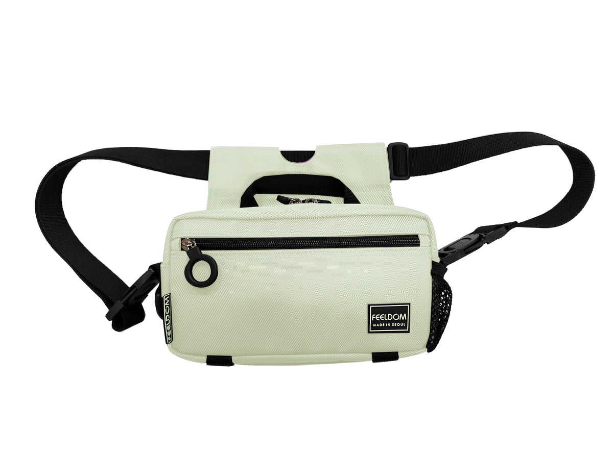An ivory colored adaptable  crossbody bag with black trim and black zipper rings. The bag's strap is configured in wheelchair / walker mode.