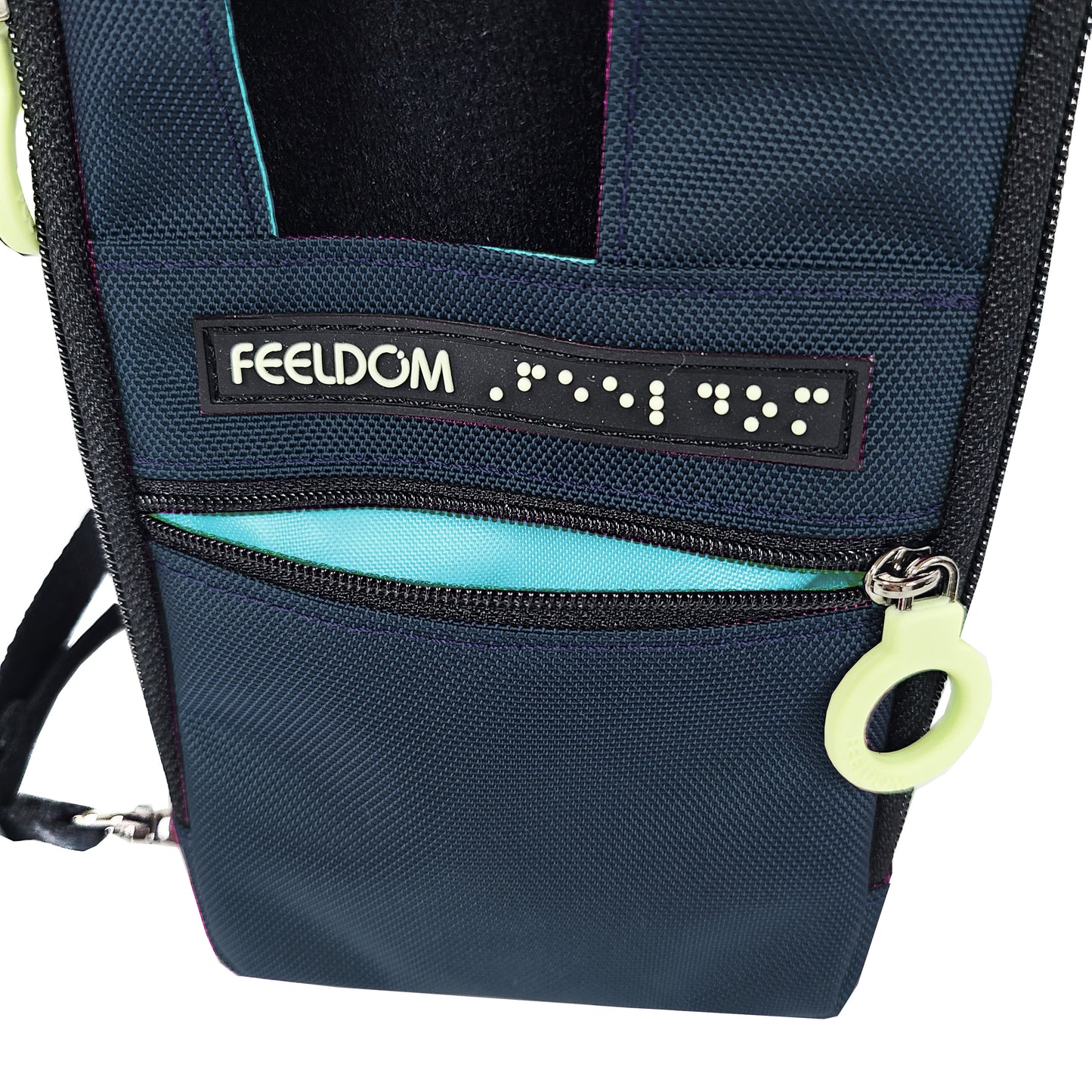 Close up detail of the front of the Navi Pal, Navy blue with an aqua lining on the front zipper pocket, which has a white zipper ring. There's a Braille Logo label above the zipper pocket