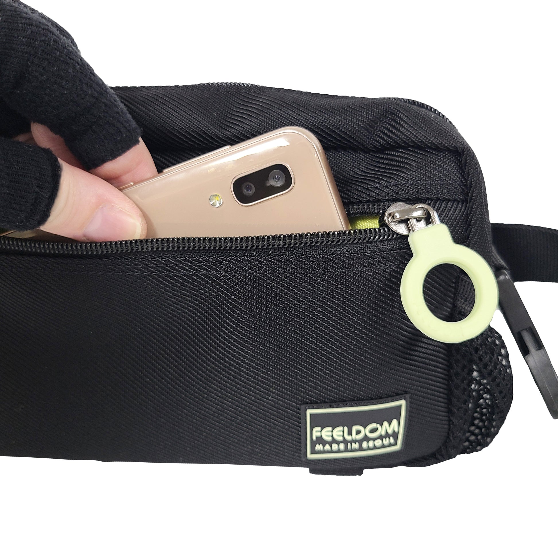 Close up of a phone being put into the front zipper pouch of a small black bag.