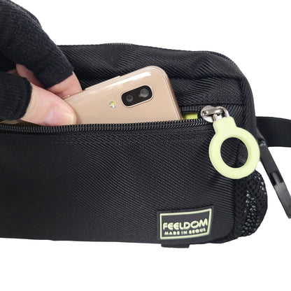 Close up of a phone being put into the front zipper pouch of a small black bag.