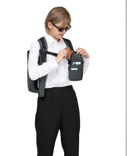 A person wearing the Performance Block backpack and the Quik-E pouch is attached to the front strap. The person is taking out the sunglasses from the case and there is a phone and ID card in the front pocket of the case.