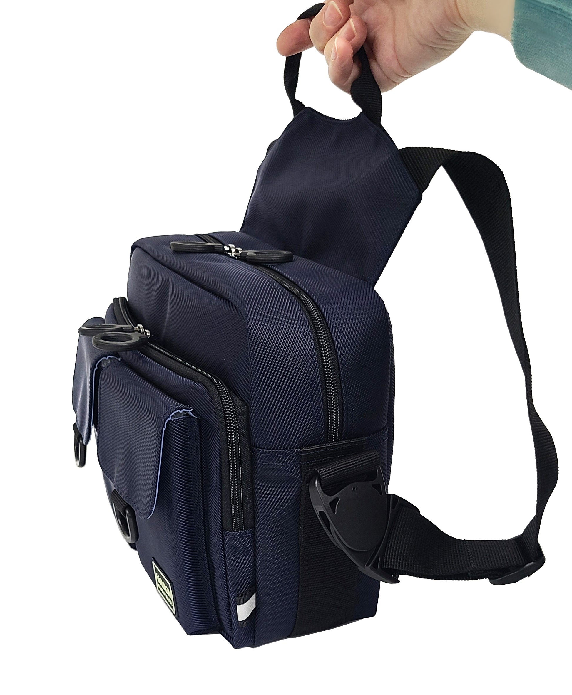 The CHIC LT24 Small bag is being put into wheelchair mode, with the two wheelchair straps taken out and buckled into the side buckles. A hand is reaching out and picking up the bag by the handle which is located on the wheelchair bag strap panel on the back.