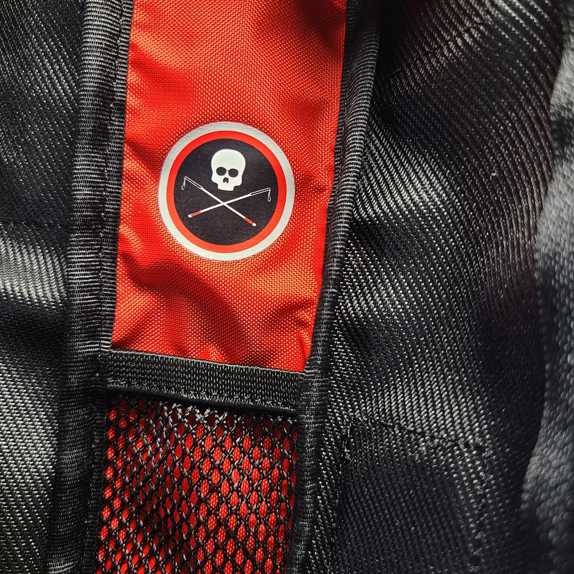 Inside detail of the black cane pouch showing a close-up of black textured fabric with a bright red vertical panel and a circular black-and-white skull logo patch.  A tiny mesh pocket is inside the center.