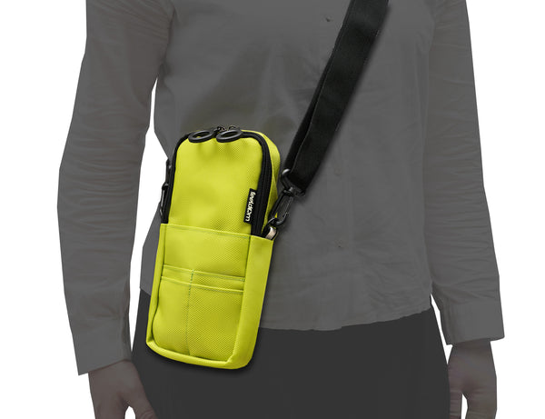 A silhouette of a person wearing a bright yellowish green rectangular mini pouch with a black wide strap, sling across the torso. The pouch has black ring zippers and slots on the front for cards and a phone or eyewear. There is a small glow in the dark FEELDOM logo in the side seam, and a reflective tab.