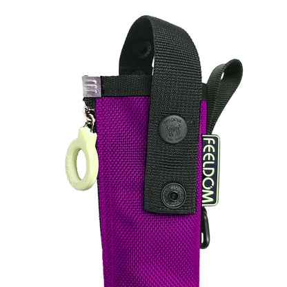 Close-up of a purple nylon cane pouch with a black webbing strap, snap button, and a small white zipper ring, and a small glow in the dark vertical tag reads FEELDOM.