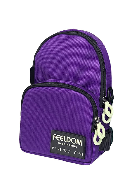 A Small Purple crossbody bag with black trim and a black and white braille logo patch on the bottom front. It has white zipper rings and a contoured front pocket