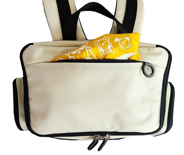 Top view of the closed City Block backpack in Arctic White with black trim and zipper rings. The top has an outer zipper pouch which is unzipped to reveal a yellow raincover folded up inside. The rain cover has Feeldom disability-inclusive doggie characters on it in a glow in the dark design.