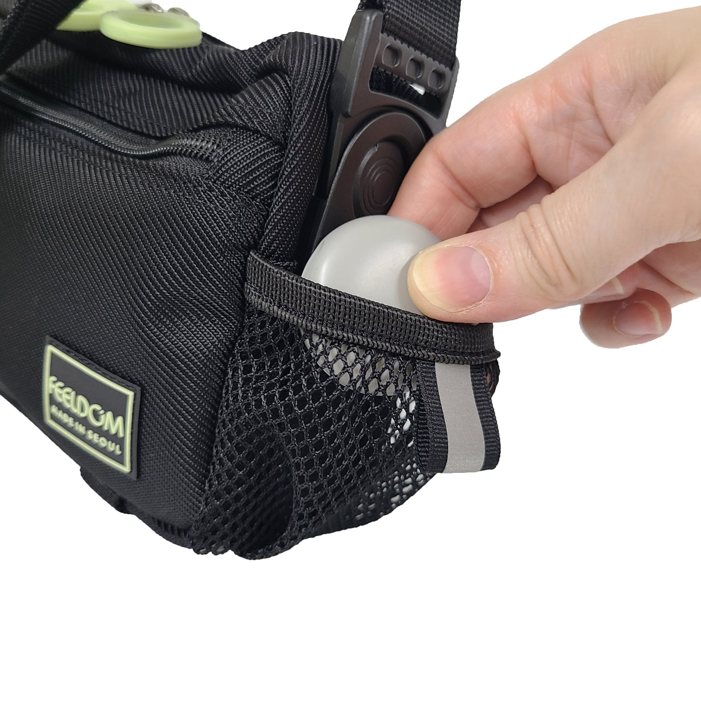 Close up of an earbud case being put into the small mesh pouch on the side of a black crossbody bag.