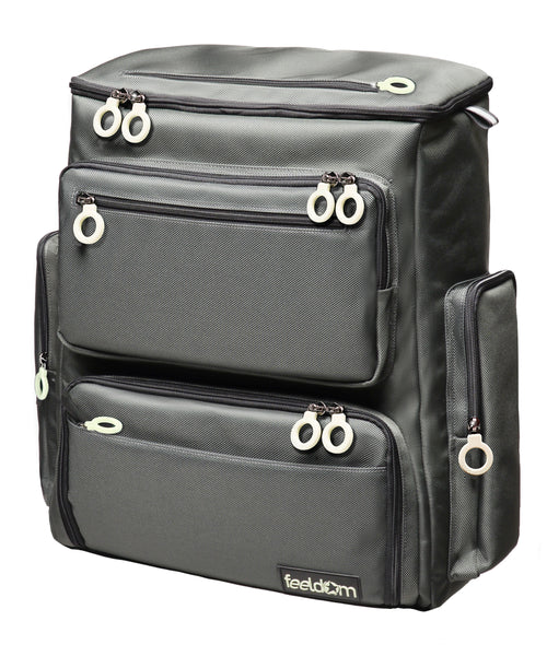 A large charcoal gray box shaped Trek Backpack with  6 outer pockets and white ring zippers on all the pockets. It has a rigid construction that is self standing, like a box.