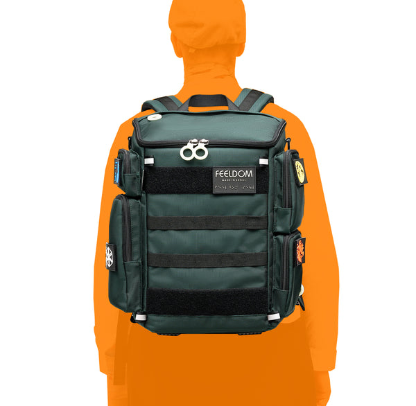 A silhouette of a person wearing a FEELDOM Cilty block dark green boxy backpack with cool tactical patches and black webbing straps on it. The top is a trapezoid angle and it opens like a box. There are bright white ring zippers and reflective tabs on the top and bottom.