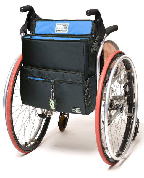 A square -shaped bag attached to the back of a manual wheelchair. It is navy blue with a sky blue lining. It has zipper side pockets that can hold a container. The clips that attach the straps are rotating push botton buckles, like a seatbelt