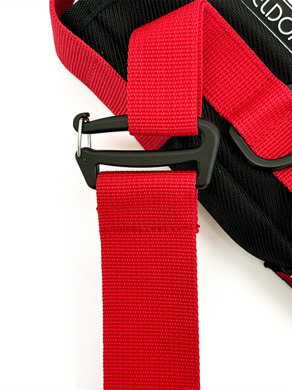 Close-up of a red webbed strap with a black plastic buckle attached to a black textured pouch.