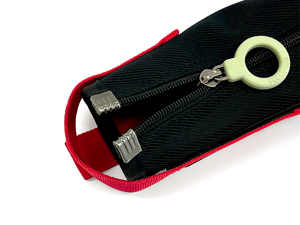 Close-up of a black zippered pouch with red trim and a greenish white ring pull and metal reinforcements on the corners of the top of the zipper.