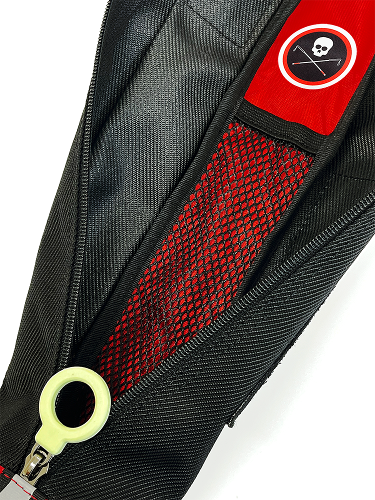 Close-up of a black zippered bag, open, with a small mesh pocket inside, a red patch featuring a white skull and crossbones logo, and a greenish white circle-shaped zipper pull.