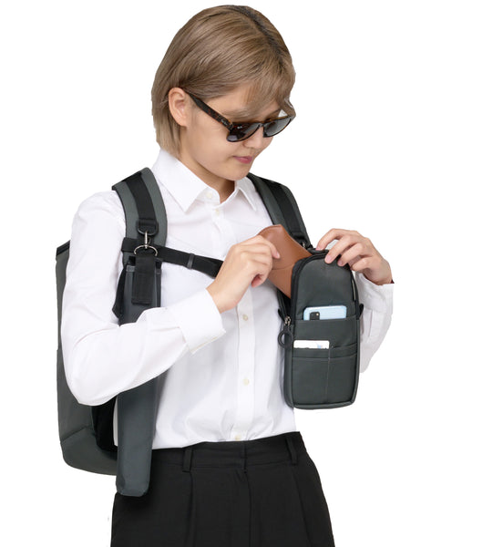 A person wearing the Performance Block backpack and the Quik-E pouch is attached to the front strap. The person is taking out the sunglasses from the case and there is a phone and ID card in the front pocket of the case.