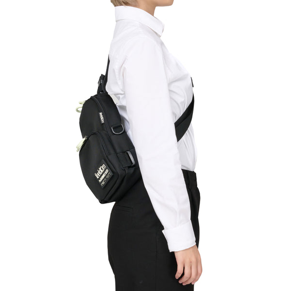 Side view of a person wearing a black crossbody bag along the lower part of their back.  The strap runs across their chest.