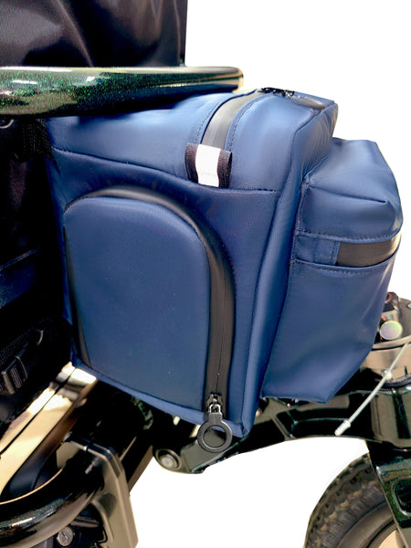 Buddy Sport Cooler attached to the back of a wheelchair. Dark blue waterproof nylon insulated block-shaped cooler with arch-shaped zipper access points on Left, Right and top.  Front pocket is also waterproof. Reflective tabs and black zippers.