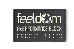 Close up of Feeldom and Performance Block Braille patch. Design is raised white (Glow in the Dark) on a black rubber rectangular patch. Feeldom logo has a star for the O.