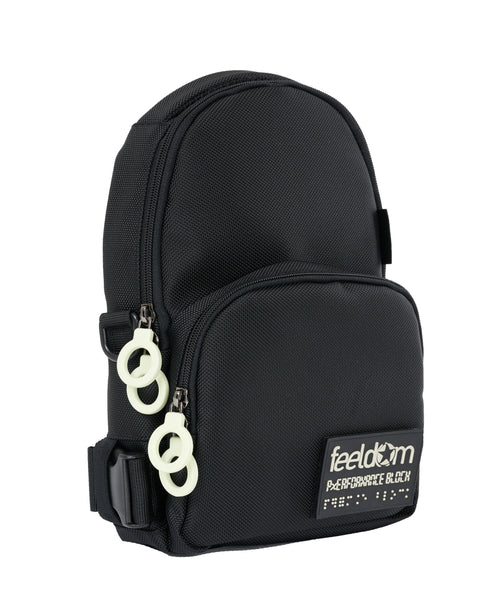 Front angle view of a black crossbody bag that has an arched top  and a smaller zipper pouch on the front which covers the bottom half. It has double white zipper rings each pocket, and a glow-in-the-dark Feeldom Logo patch on the front which is removable by velcro.
