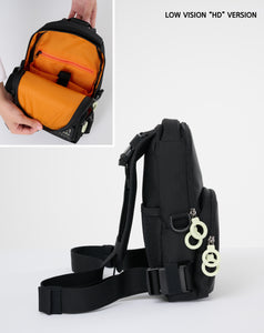 Details of the "Low-vision H.D. version" crossbody bag that has black outside, bright orange lining, and white zipper rings, glow-in-the-dark logo patch.