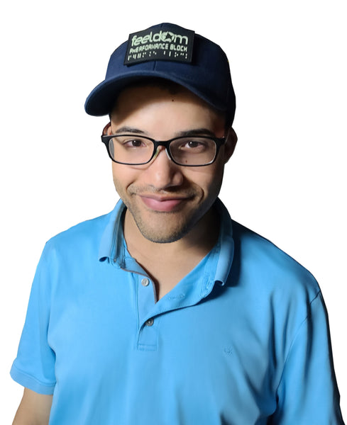 Young guy with black glasses is wearing a sky blue polo shirt and a navy blue ball cap. The cap has a Feeldom Performance Block Tactical patch applied to the front. 