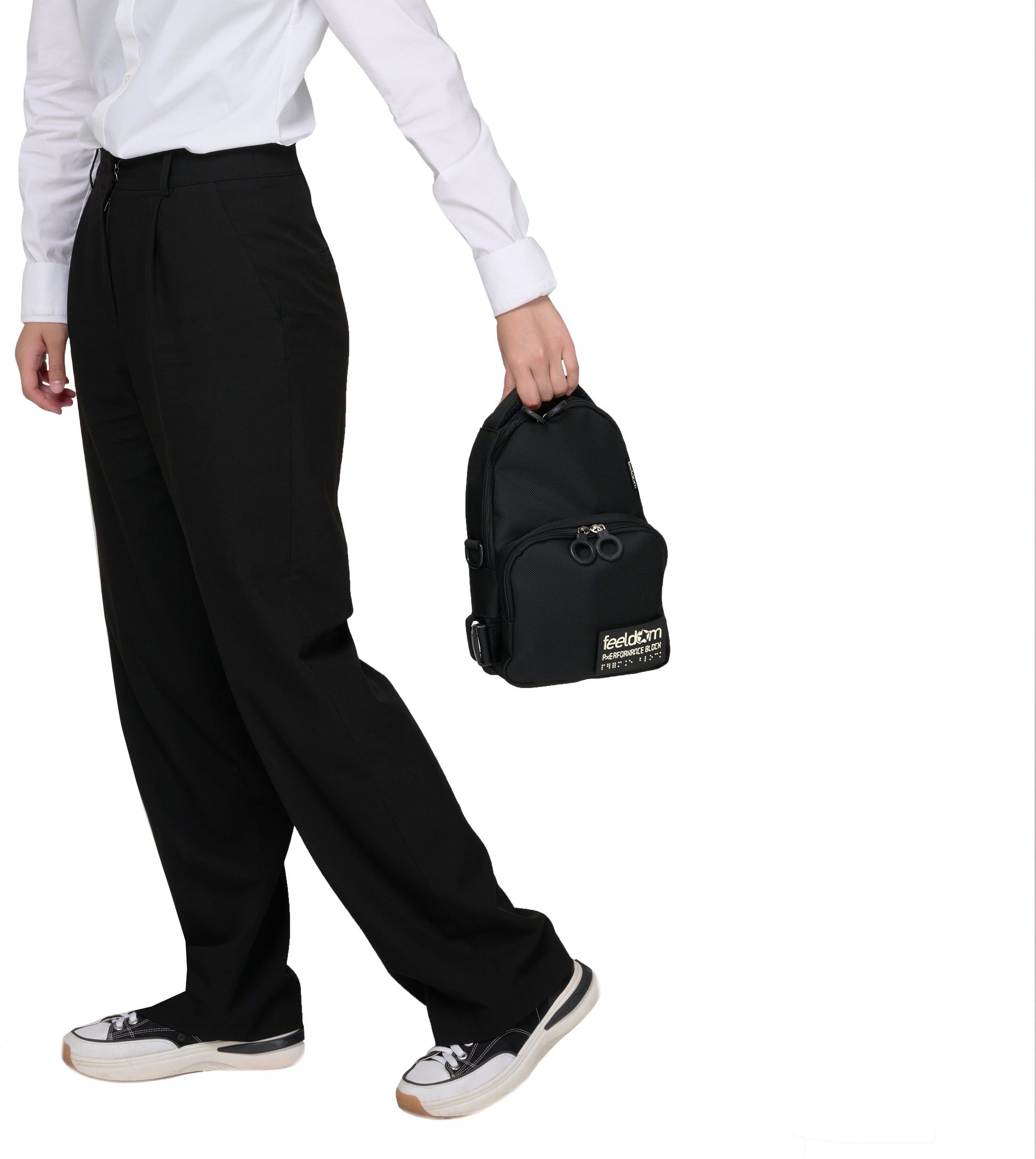A person walking away while holding the padded top handle of the black crossbody bag. The shoulder/chest strap has been removed completely, so now it looks like a mini satchel.