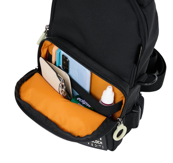 Close up view of the front pouch of the Black crossbody bag which is zipped open and folded down to show the bright orange lining. There is a black elastic strap which runs across the back wall of the pocket, so that the cell phone and eyedrops, pens, will remain upright and not fall out easily. There is a wallet and mints also stored in there with plenty of room for more stuff.
