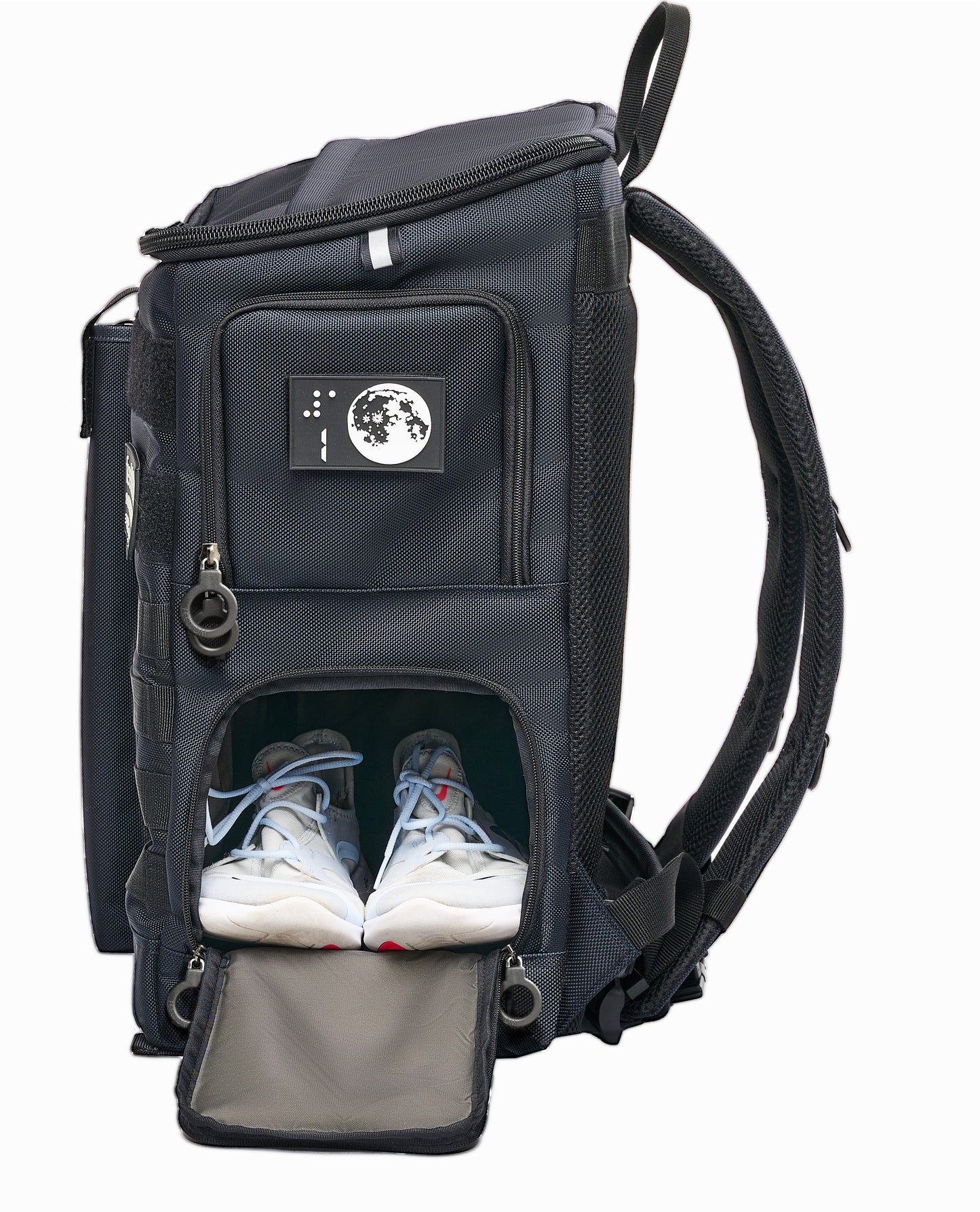 Side view of Navy Blue with open bottom compartment. White athletic shoes are in there, side by side. Top compartment is zipped closed. It has a white moon design braille patch with the number 1 on it.
