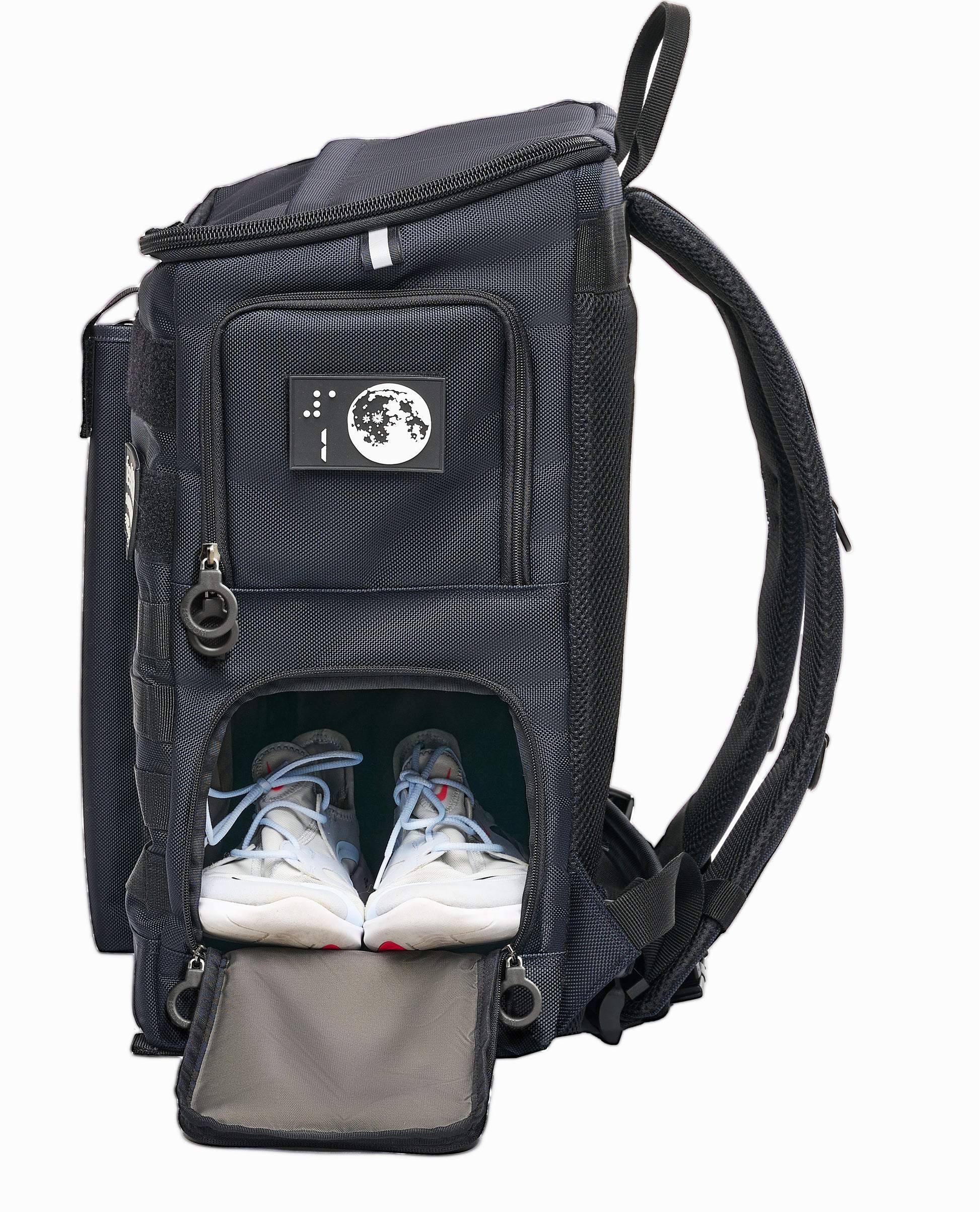 Side view of Navy Blue with open bottom compartment. White athletic shoes are in there, side by side. Top compartment is zipped closed. It has a white moon design braille patch with the number 1 on it.