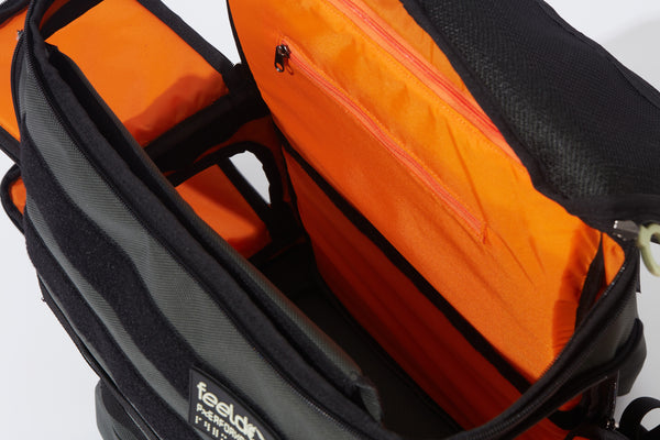 Inside view of a Large backpack with bright orange lining and a divider for the upper and lower compartments. Side openings are on the right and left.  The top lid opens for a 13 inch Laptop computer and under the lid is a mesh zipper pocket.