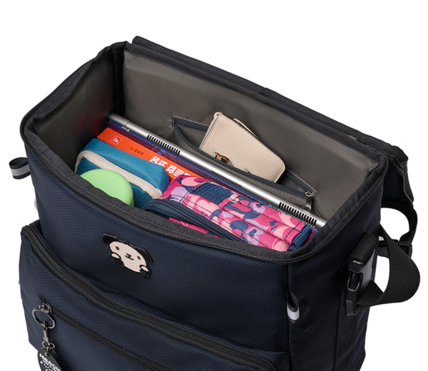 A box shaped navy blue wheelchair bag with the flip top lid open. Inside is a lunchbox, tablet PC, Pencil case, thermos and some books. A wallet is in the small pocket