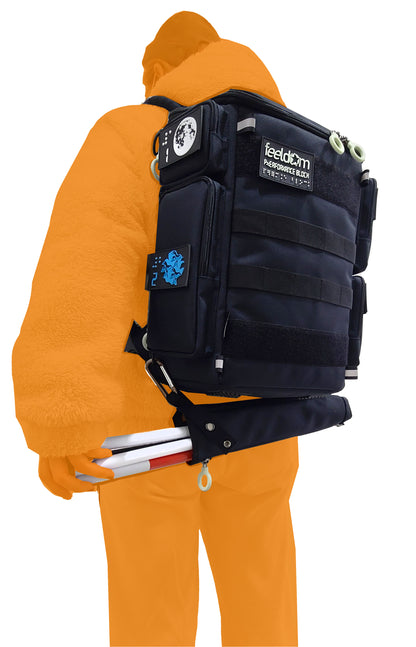 A person wearing the CITY BLOCK backpack with the cane pouch attached horizontally underneath the backpack, via carabiner and clip. The person is reaching behind to easily remove the cane from the pouch.