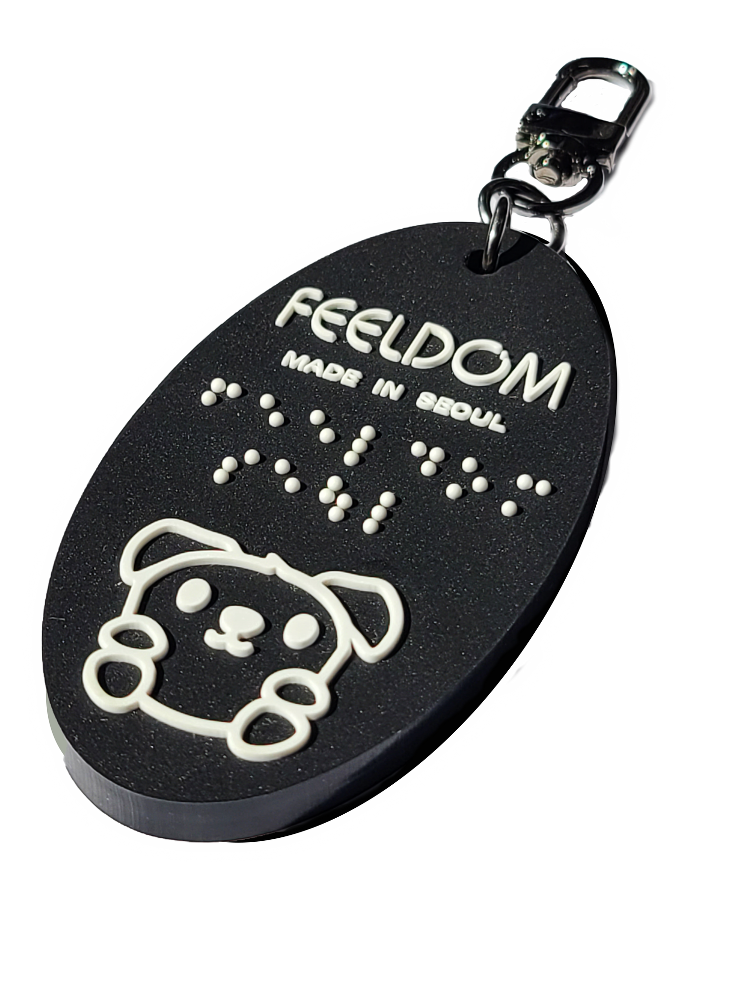 Feeldom's mascot, Goldie the service pup, is the character on our Black rubber oval-shaped keyfob. The white lettering "Feeldom, made in Seoul" are also in Braille (white). It has a 2-inch dark nickel chain and U-shaped clip for versatile use. 